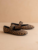 Pair of leopard print shoes with decorative buckles on a beige background
